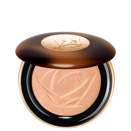 A imagem mostra o sérum iluminador Lancôme. A embalagem é redonda com tampa marrom e logotipo dourado no centro. A parte inferior preta com aro dourado. Interior contém o pó iluminador bege com padrão rendado.