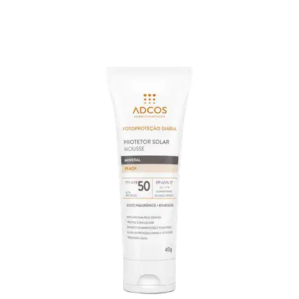 Protetor solar mousse mineral da marca Adcos, embalagem plástica branca e tubo de 40g. Fórmula com FPS 50, proteção UVB e UVA 17. Cor pêssego. Contém ácido hialurônico e bisabolol. Indicado para peles sensíveis. Resistente à água.