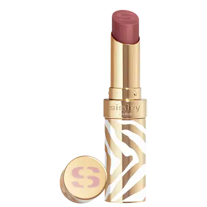 Bálsamo labial em embalagem dourada com detalhes brancos e marrons em padrão zebrado. A cor do hidratante é marrom vinho. O rótulo "Sisley Paris" está visível na embalagem dourada. Há também um pequeno espelho compacto dourado com o logotipo "S".
