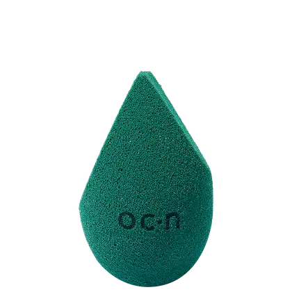 Esponja de maquiagem verde escuro com textura aveludada. Formato de gota com a palavra "Océane" impressa em relevo na superfície.