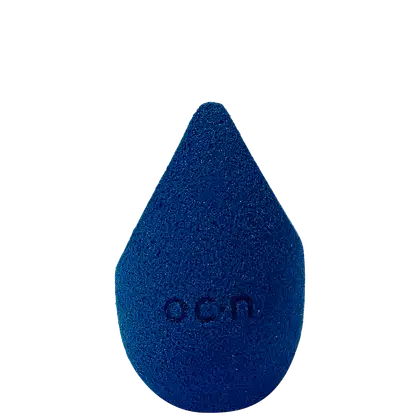 Esponja de maquiagem azul escuro com textura aveludada. Formato de gota com a palavra "Océane" impressa em relevo na superfície.