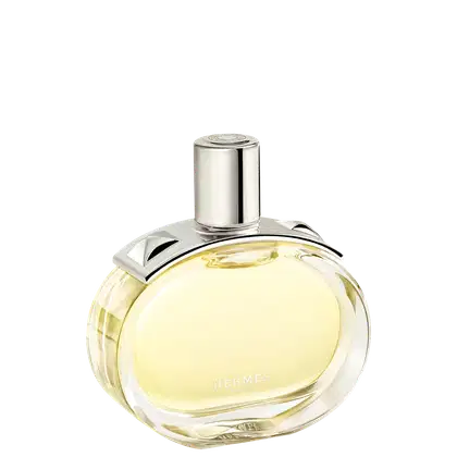 A imagem mostra o perfume Barénia de Hermès. Seu frasco é de vidro arredondado e transparente, permitindo ver o líquido amarelado em seu interior. Sua tampa é cilíndrica e prateada e possui uma aplicação com pinos em forma de pirâmide com facetas curvas.
