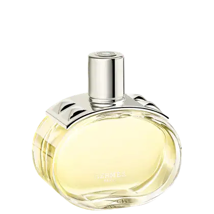 A imagem mostra o perfume Barénia de Hermès. Seu frasco é de vidro arredondado e transparente, permitindo ver o líquido amarelado em seu interior. Sua tampa é cilíndrica e prateada e possui uma aplicação com pinos em forma de pirâmide com facetas curvas.