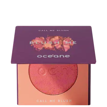 A imagem mostra o produto Blush Me da marca Océane. É uma embalagem quadrada de cor roxa que está semiaberta mostrando a cor do blush em um tom laranja com leve brilho perolado. A parte interna da embalagem é de cor pêssego claro,
