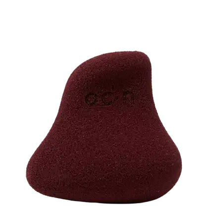Esponja de maquiagem facial em formato de gota, com textura porosa e cor vinho escura. O produto possui uma aparência aveludada e macia. Não há rótulos ou texto visível.