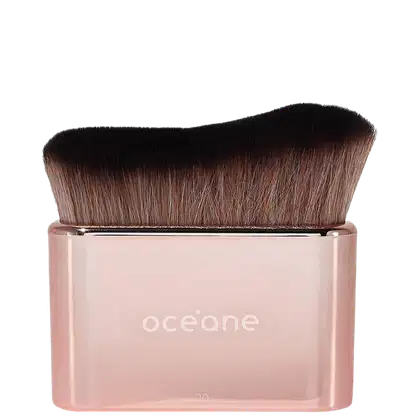 Pincel de maquiagem com cerdas macias e densas de cor castanha escura. Cabo transparente de plástico rosa claro com o nome "oceane" impresso em letras minúsculas brancas.