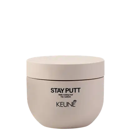 A imagem mostra a pasta finalizadora Stay Putt da marca Keune. Um pote arredondado bege claro fosco com tampa da mesma cor. Está impresso em letras pretas "STAY PUTT Matte molding mud Pâte matifiante".