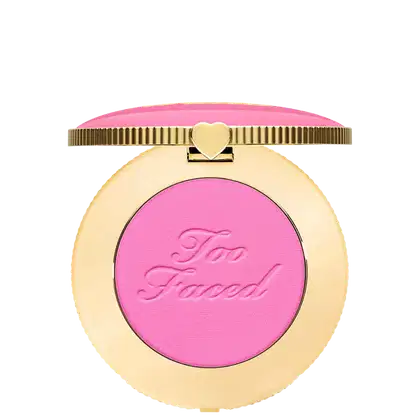 Blush compacto de maquiagem com embalagem redonda dourada. A tampa superior é rosa com a inscrição "Too Faced" em letras cursivas. Um pequeno coração dourado adorna o centro da tampa.