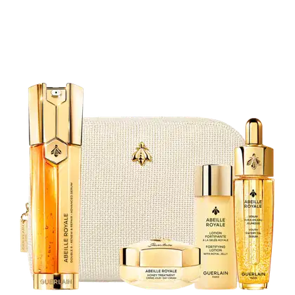Conjunto de itens de perfumaria da marca Guerlain, incluindo frascos dourados, caixa bege com textura, e rótulos com o nome da marca e da linha "Abeille Royale". Os produtos parecem ser soros, loções e cremes para cuidados com a pele.