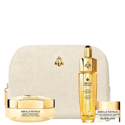 Conjunto de produtos de beleza Abeille Royale da marca Guerlain. Inclui frasco de sérum de óleo aquoso, pote de creme hidratante e embalagem acolchoada bege. Todos os itens apresentam detalhes dourados, como tampa e logotipo da abelha.