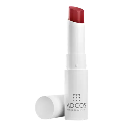 Bálsamo Hidratante Labial com embalagem branca com tampa e logotipo da marca Adcos Dermocosmética em cinza. O bálsamo possui uma cor vermelha escura e brilhante.