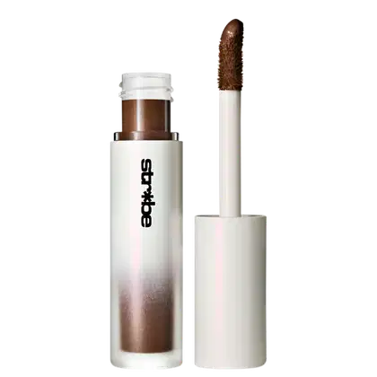 Produto de maquiagem em embalagem branca e marrom, com rótulo preto exibindo a marca "Strobe". O produto parece ser um aplicador de maquiagem com uma escova marrom em uma extremidade.