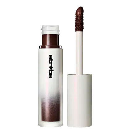 Frasco branco e marrom de um produto de maquiagem da linha Strobe de MAC, contendo um aplicador de ponta escura. O produto parece ser um item de maquiagem, possivelmente um batom ou gloss labial.
