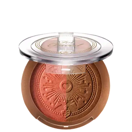 Pó bronzeador compacto em embalagem redonda de plástico transparente, com detalhes dourados e um desenho de sol estampado no centro. O produto possui uma tonalidade dourada brilhante.