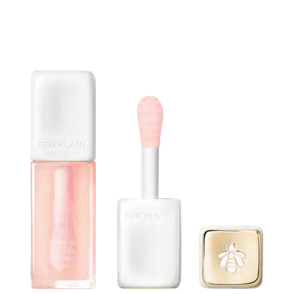 Frasco Lip Oil Guerlain de cor rosa, pincel aplicador branco e caixa dourada com abelha, apresentando uma linha de produtos de beleza da marca.