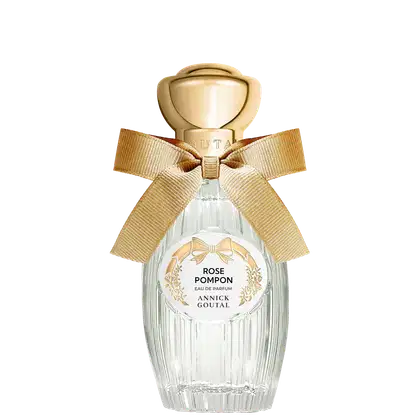 Eau de Parfum Rose Pompon Annick Goutal em frasco de vidro transparente com tampa dourada esférica, laço de fita bege e rótulo circular branco com detalhes florais dourados.