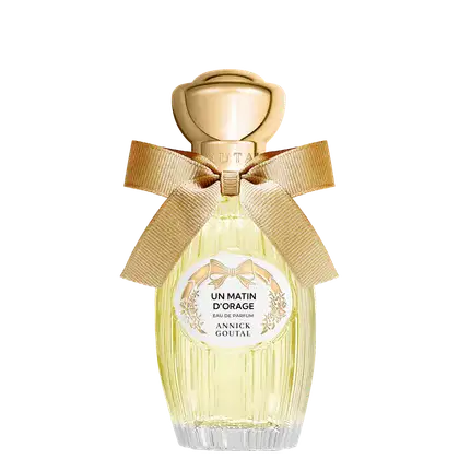 Eau de Parfum Un Matin d'Orage da Annick Goutal em frasco de vidro amarelo claro com tampa dourada esférica, decorado com laço de fita bege e rótulo circular branco com detalhes florais dourados.
