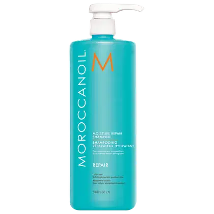 A imagem mostra o Shampoo Moroccanoil Repair Moisture 1L, um frasco de plástico azul turquesa e com uma bomba dosadora branca na parte superior. O logo traz um M em tom de laranja e o nome da marca em branco.