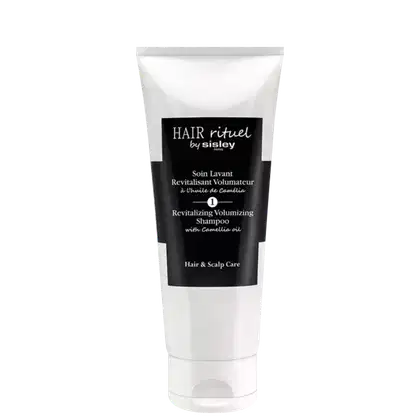 Tubo branco com rótulo preto e branco contendo texto "Hair rituel by sisley" e "Revitalizing Volumizing Shampoo with Camellia oil". O produto é um item de cuidados capilares da marca Sisley.
