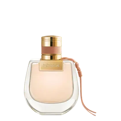 Perfume em frasco de vidro transparente com formato arredondado. A tampa é dourada com detalhes em couro rosé. O nome "NOMADE" está gravado em letras douradas na parte superior da tampa. O líquido dentro do frasco é de uma tonalidade bege claro.