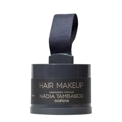 Embalagem preta com rótulo "Hair Makeup" da marca Océane, contendo maquiagem capilar da designer Nádia Tambasco. Recipiente com tampa e alça de tecido preto, apresentando informações sobre o produto em destaque.