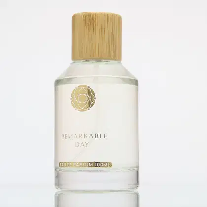 Frasco de perfume Remarkable Day da marca Kiyomi, com 100ml de capacidade, embalagem de vidro transparente e tampa de madeira, com rótulo dourado e branco destacando o nome do produto.