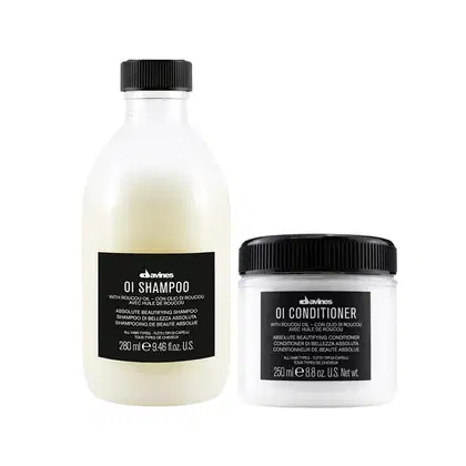 Dois produtos Davines: um frasco de shampoo com rótulo preto e branco, e um pote de condicionador com rótulo semelhante. Ambos contêm óleo de roucou e são descritos como "Absolute Beautifying" para todos os tipos de cabelo.