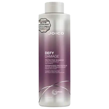 Frasco de shampoo Joico Defy Damage, com embalagem branca e roxa, contendo informações sobre o produto e selo de originalidade. O produto é descrito como um shampoo protetor para fortalecimento e prolongamento da cor.