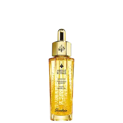 A imagem mostra o frasco do óleo hidratante Abeille Royale da Guerlain. É um frasco de vidro transparente contendo um líquido dourado brilhante, tem um formato cilíndrico alongado com uma tampa dourada na parte superior, com uma abelha estampada.