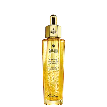 A imagem mostra o frasco do óleo hidratante Abeille Royale da Guerlain. É um frasco de vidro transparente contendo um líquido dourado brilhante, tem um formato cilíndrico alongado com uma tampa dourada na parte superior, com uma abelha estampada.
