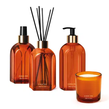 Quatro itens da marca Casa 214 Vanilla Sublime em vidro laranja, sendo um difusor de ambiente com varetas, um aromatizador de ambiente em spray, um sabonete líquido com bico dosador e uma vela perfumada.