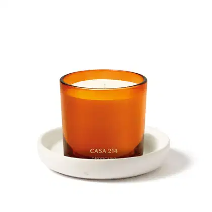 Vela perfumada da marca Casa 214 Vanilla Sublime em recipiente laranja e vela branca aromatizada acompanhada de um suporte para velas na cor branca.