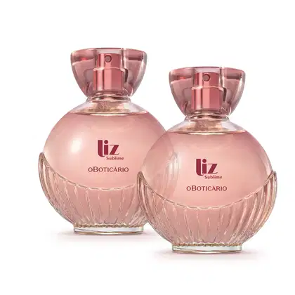 Dois frascos de item de perfumaria da marca Liz Sublime, com embalagem de vidro arredondada rosa-claro facetado e nome da marca em vermelho escuro gravado no vidro. A tampa é em acrílico transparente e permite ver a tampa borrifadora de tom metálico rosa.
