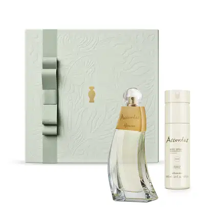 Caixa de presente prateada com laço cinza e detalhe dourado, vidro curvilíneo com detalhe dourado de desodorante colônia Accordes e body splash em embalagem branca com letras marrom da mesma marca.