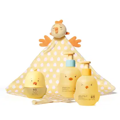 Combo de produtos de higiene infantil Boti Baby, sendo um frasco de shampoo, um de sabonete líquido e uma colônia infantil, todos com formato de pintinho amarelo. Acompanha naninha atoalhada amarela de bolinhas brancas e pelúcia de galinha na ponta.