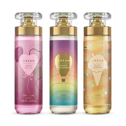 Imagem de três frascos de body splash Dream: um com rótulo roxo da linha Amor no Ar, um com rótulo colorido da linha Viagem Encantada e outro com rótulo dourado da linha Céu de Baunilha. As embalagens são de vidro com válvula spray dourada.