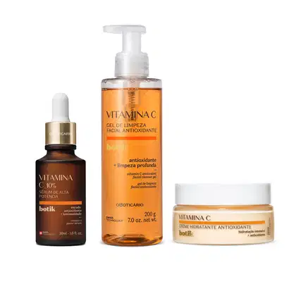 Imagem de três produtos de cuidados com a pele da marca Botik: sérum de vitamina C em frasco marrom com conta-gotas, gel de limpeza facial em embalagem transparente e conteúdo laranja e creme hidratante facial em um pote branco com detalhes laranja.