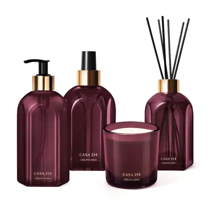 A imagem mostra um kit com quatro itens da linha Casa 214 Figo Magnífico: sabonete líquido, aromatizador de ambiente, vela perfumada e difusor de ambiente. Todos eles são em vidro roxo com detalhes em dourado e preto. Acompanha varetas de madeira.
