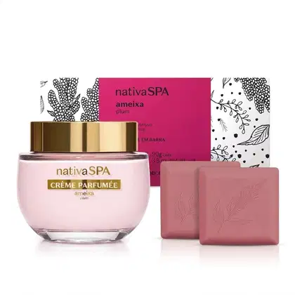 Embalagem de sabonete em barra da linha Nativa SPA Ameixa branca com detalhes ilustrados em preto e rótulo pink com informações sobre a marca. A frente dela, pote de creme perfumado de vidro com tampa dourada e 2 sabonetes em barra rosa quadrados