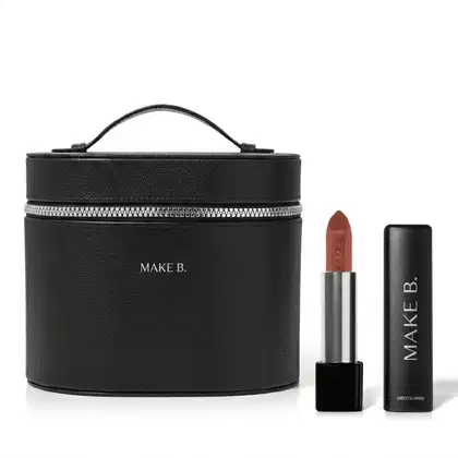 Frasqueira de maquiagem preta com zíper e alça, com aspecto rígido e estruturado feita em tecido tipo couro e logo Make B. em hot stamping prata e um batom nude aberto com a bala visível, corpo prateado e base preta com tampa preta ao lado.