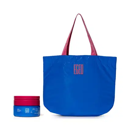 Imagem de uma bolsa grande azul com alças rosa e logotipo da marca Egeo, acompanhada de um pote azul com tampa rosa da mesma marca,, contendo um creme hidratante corporal.