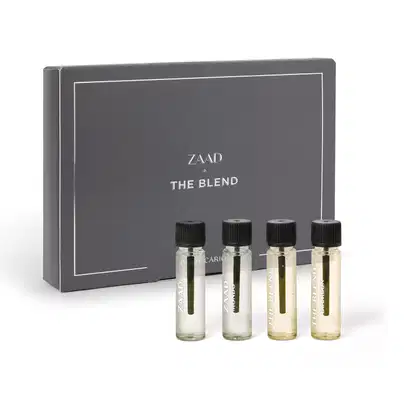 Caixa cinza com detalhes e letras branca ao lado de quatro frascos transparentes com líquidos claros e tampas pretas de miniaturas dos itens de perfumaria masculina O Boticário, sendo elas Zaad, Zaad Mondo, The Blend e The Blend Bourbon.