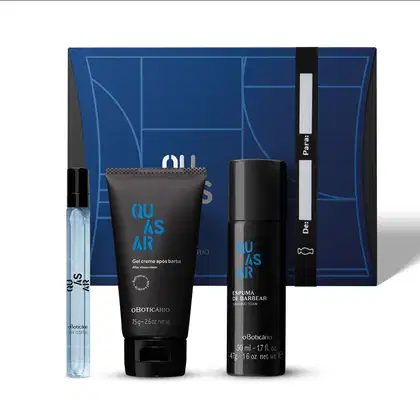 Quatro produtos Quasar, sendo uma caixa de presentes com ilustrações geométricas, bisnaga azul escura com letras azuis e douradas de gel creme após barba, frasco nas mesmas cores de espuma de barbear e vidro cilíndrico de 10ml de desodorante colônia.