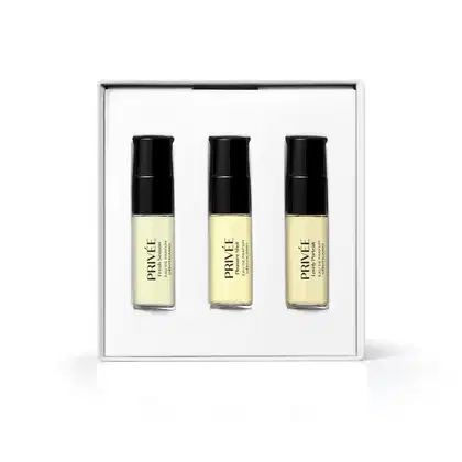 Kit de três frascos de fragrância em versão miniatura da marca Privée, em caixa branca. Os frascos são transparentes com líquido amarelado com tampa e letras pretas.