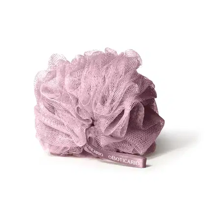 Imagem de uma esponja de banho rosa em formato arredondado, com textura de rede, com a marca "O Boticário" impressa em fita rosa. Um acessório para relaxamento e bem-estar.