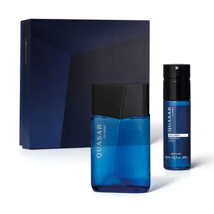 Imagem de dois produtos da marca Quasar Classic, sendo um vidro de desodorante colônia e um frasco de body splash, sendo as duas embalagens na cor azul com tampa preta e rótulo amarelo, acompanhado de uma caixa com ilustrações geométricas em tons de azul.