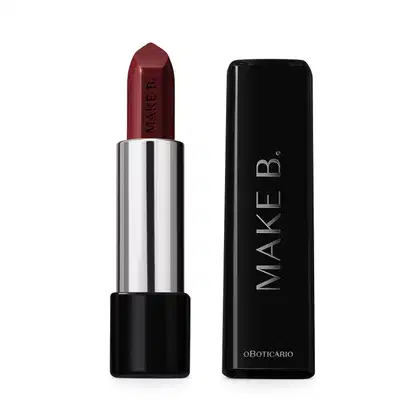 Batom em tom de vermelho escuro da marca Make B. aberto. De um lado, a tampa preta com texto em branco, com formato retangular e ponta arredondada. Do outro, a base preta, o corpo prateado e a bala de batom aparente com a marca gravada em baixo relevo.