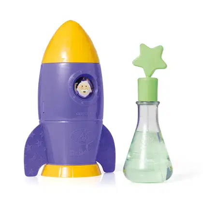 Foguete de brinquedo roxo e amarelo da marca Dr. Botica com estrelas, ao lado de um frasco de vidro verde com tampa em forma de estrela.