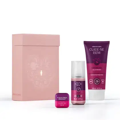 Caixa rosa claro com padrão floral em dourado e três itens de corpo e banho da marca Cuide-se Bem Amoruda, sendo um body spray, uma bisnaga de loção corporal e um hidratante labial, todos nas cores roxo e pink.
