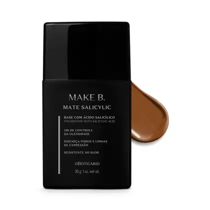 Frasco preto de base da linha Make B. Mate Salicylic com texto em branco trazendo informações do produto, como presença de ácido salicílico, controle de oleosidade e resistência ao suor. Atrás da embalagem, vemos um pouco de base bege escura espalhada.